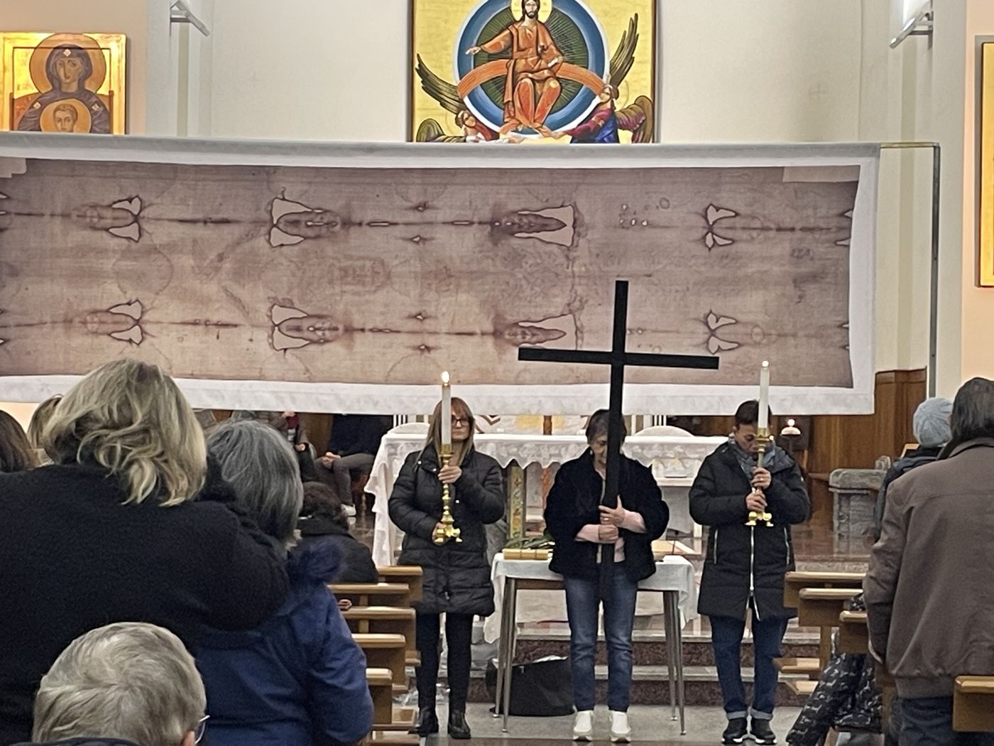 Fedeli davanti alla copia della Sindone esposta sotto il mosaico dell'abside, con la croce e due ceri